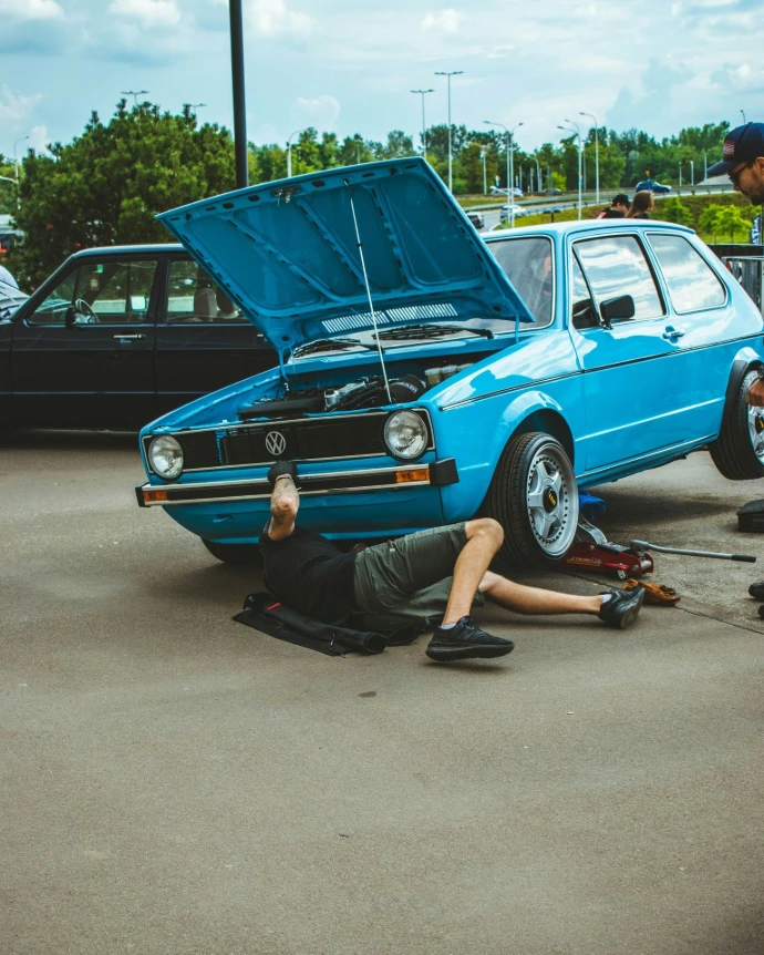 a man laying on the ground next to a blue car